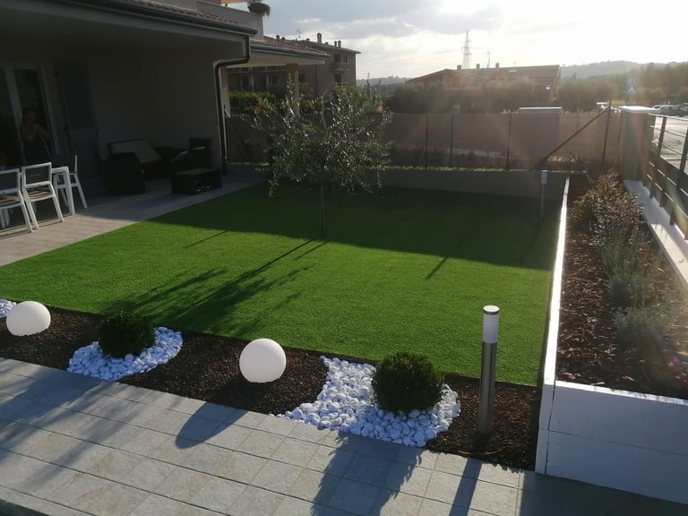 Rooftop terrace with artificial turf, decorative landscaping with blue pebbles and white spheres, potted plants, and building view