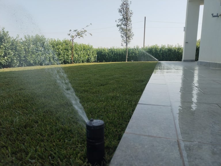 Lawn sprinkler head spraying water on green grass beside a paved patio area