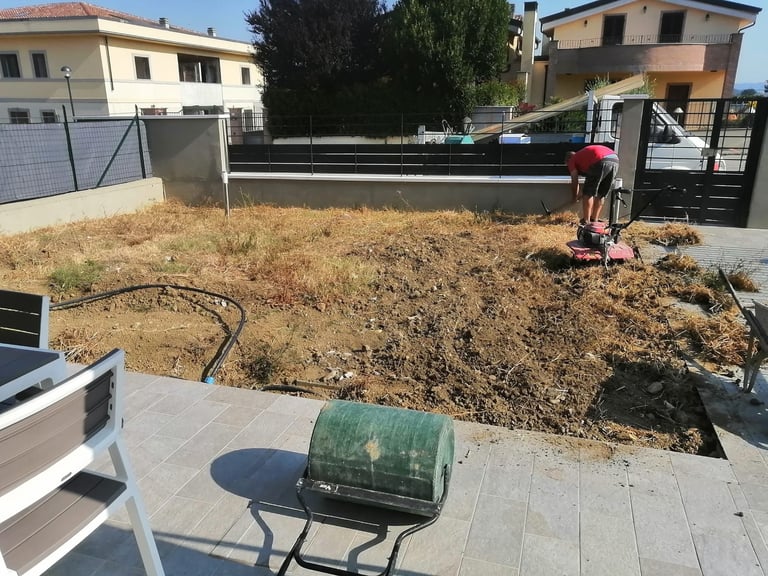 Construction site with bare earth, compacting equipment, and residential buildings in background on sunny day