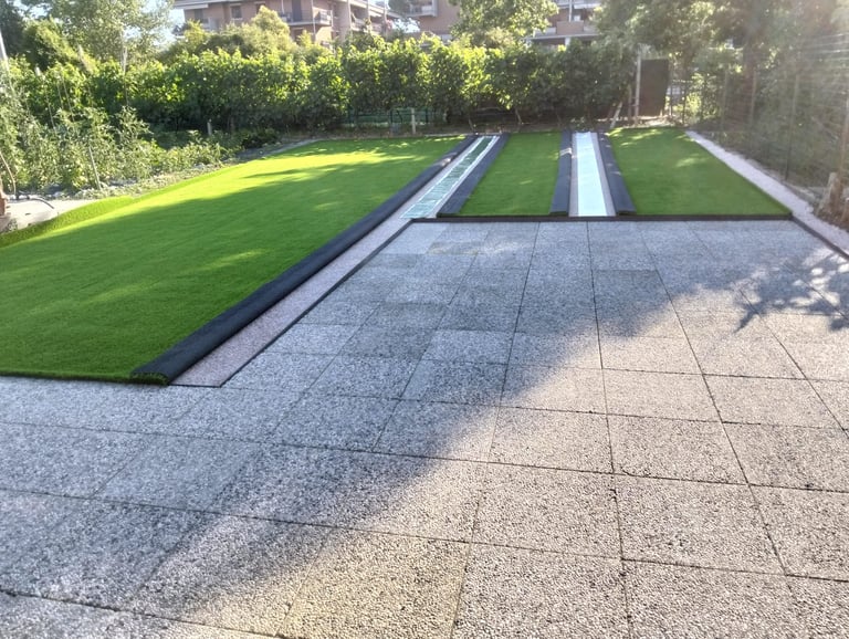Modern patio with paved flooring, artificial grass lawn sections, metal drainage channels, and urban building backdrop