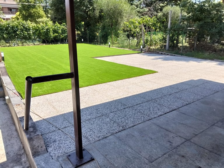 Modern backyard patio with black metal railings, paved terrace, and lush green lawn bordered by trees