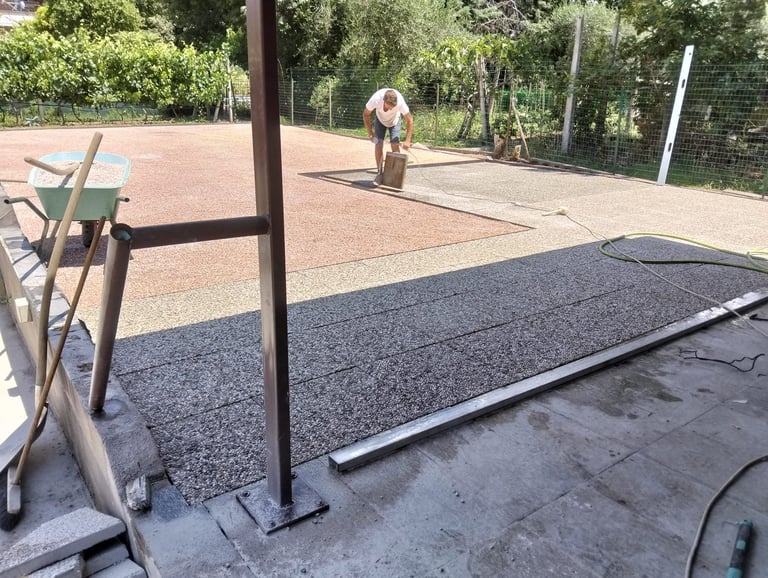 Installation of dark gray roof shingles or roofing material on a residential property with landscaping and pathway visible in background