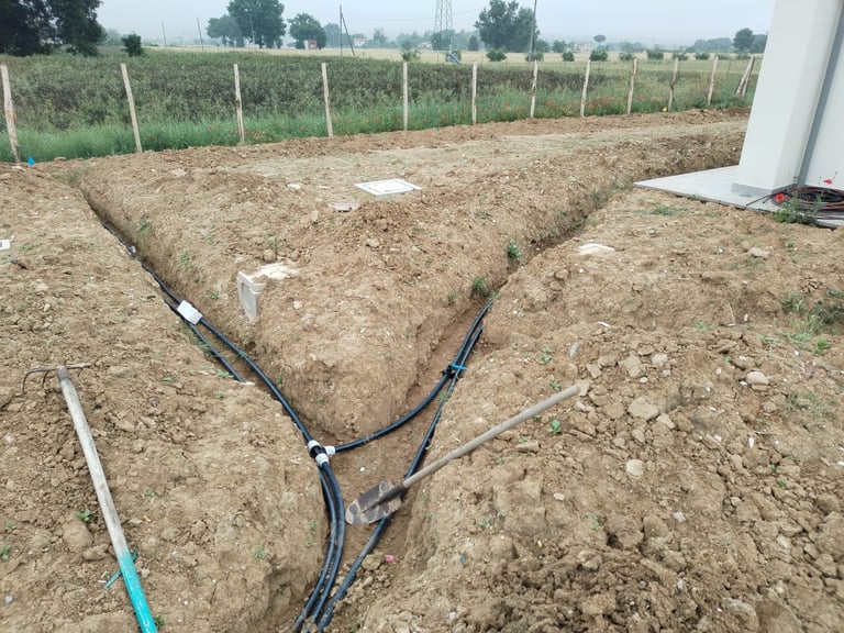 Irrigation drip lines laid in V-shaped rows in agricultural field with fencing and crops in background