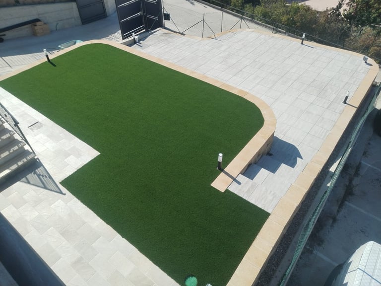 Aerial view of a rooftop with artificial turf surrounded by white pavement and tan border
